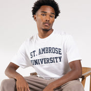 Person wearing a white t-shirt with 'St. Ambrose University' text, sitting on a chair against a plain background.