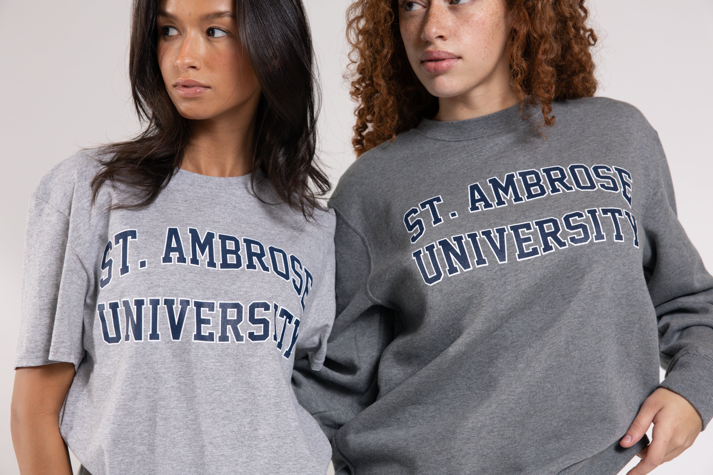Two people wearing gray 'St. Ambrose University' sweatshirts against a plain background