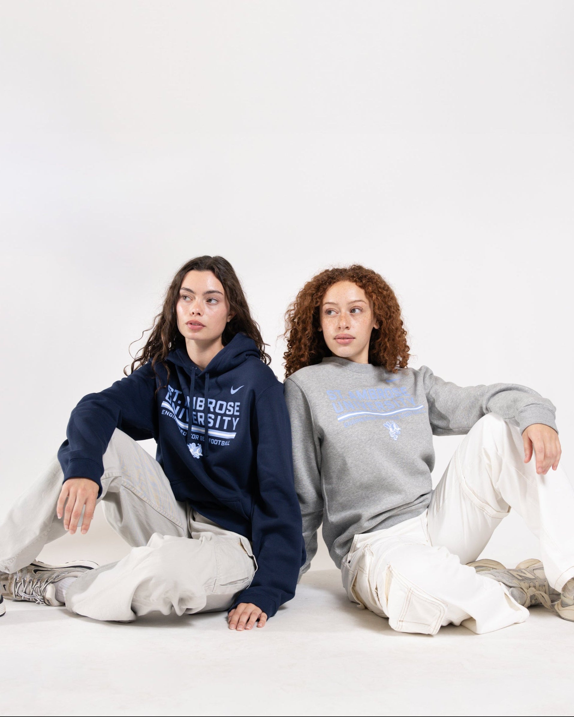 Two people wearing hoodies and pants sitting on a white background